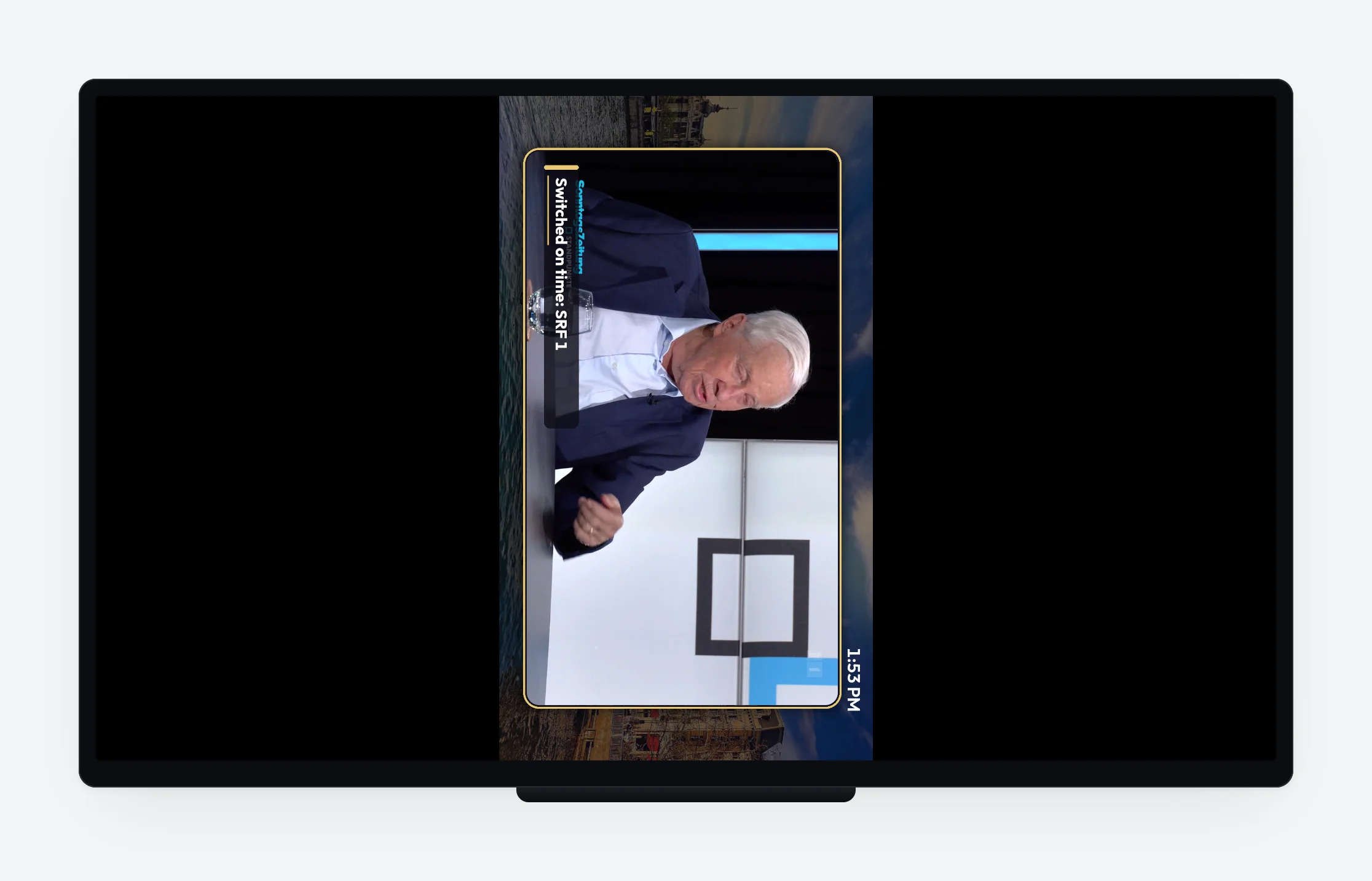 A TV mounted in portrait, its picture turned by the player, showing a live channel with a lower third.