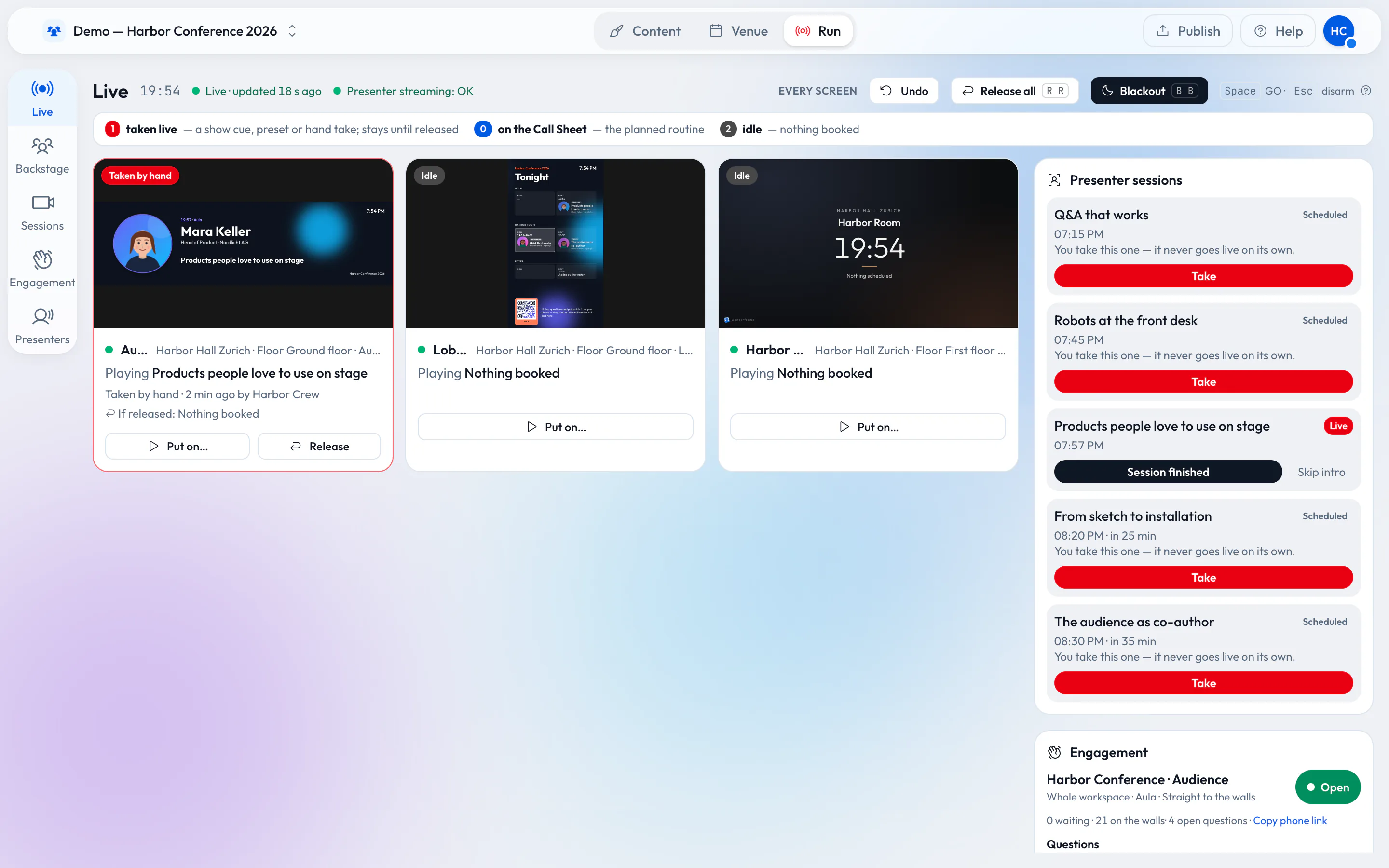 The Wunderframe Live desk: three stage cards (the Aula taken by hand with a speaker intro, the Lobby with the agenda board, the Harbor Room idle), a list of presenter sessions with Take buttons, and an open engagement with 21 posts on the walls.